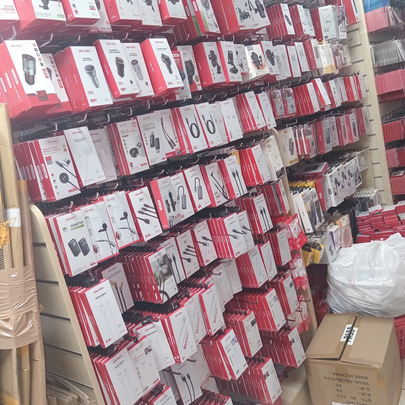 A full wall of boxed phone accessories in Techmart: car chargers, cables, adapters, earphones and power banks displayed on hooks.