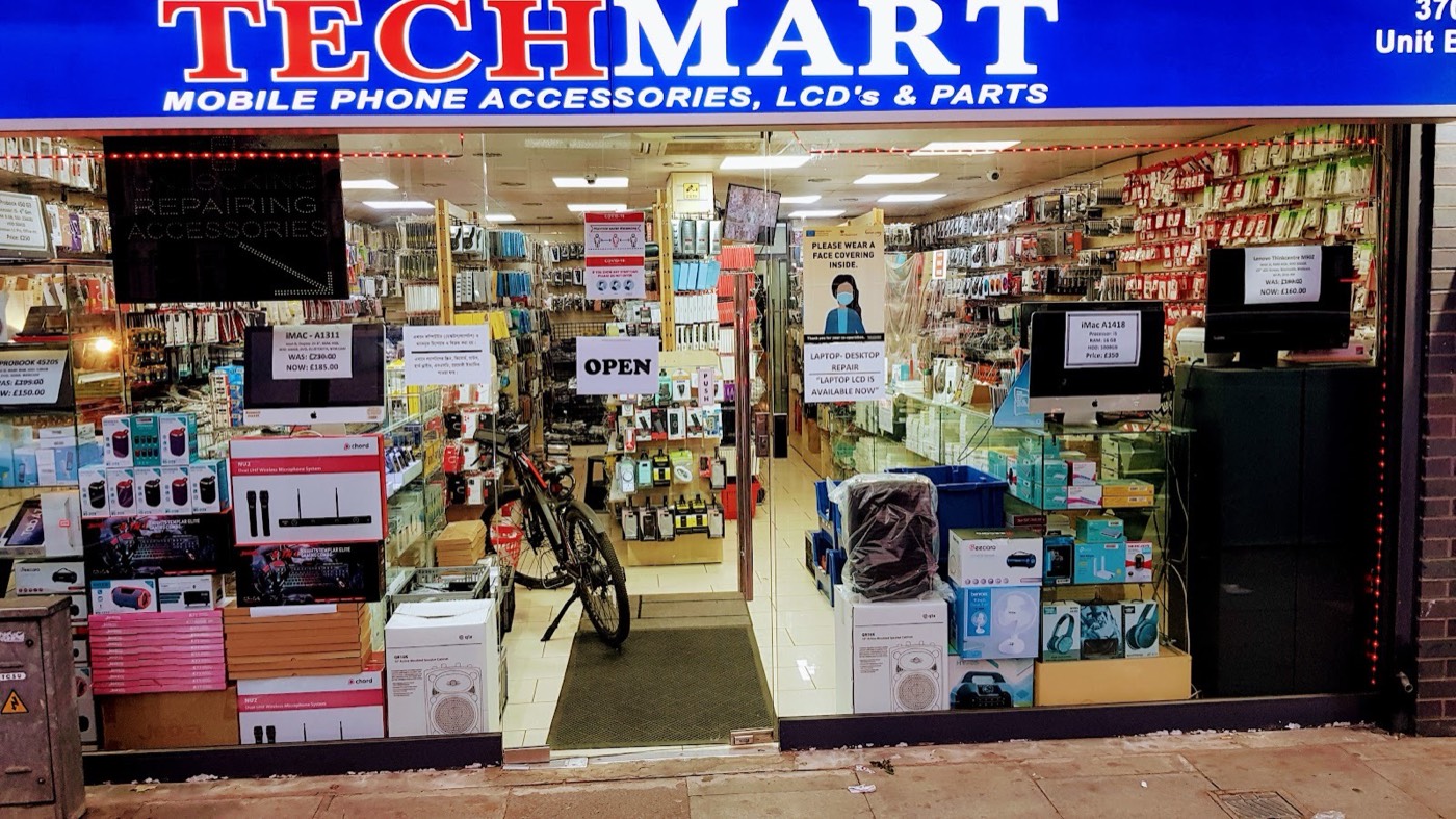 The Techmart shopfront on Romford Road, Forest Gate, its blue fascia reading Techmart, Mobile Phone Accessories, LCD's and Parts, with the shop lit up and stocked.